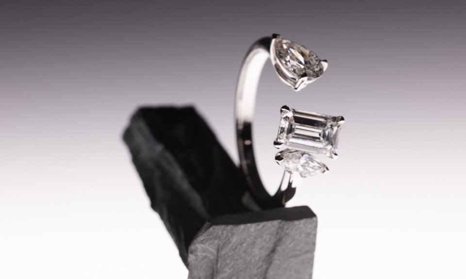 Разомкнутое кольцо, объединившее на глянцевых золотых ободках композицию из трех бриллиантов, замерло на осколках графитно-серой горной породы. Фото: ALROSA Diamonds