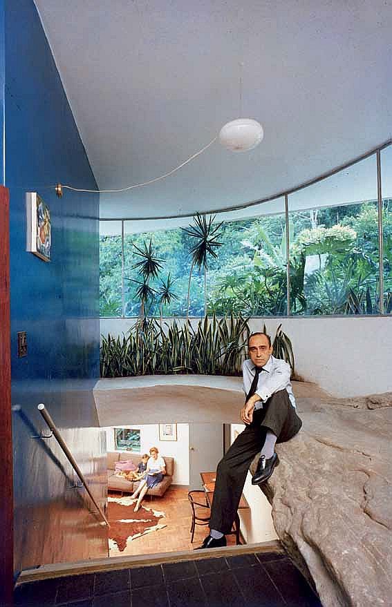 Оскар Нимейер в собственном доме, в архитектуру которого он включил фрагмент скалистой породы. Внизу, в гостиной, заняты чтением его жена и внук
