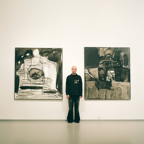 Евгений Музалевский на фоне своих работ. Персональная выставка «Монохром, с мамой за спиной» в МАММ (2024). Фото: Аlina Pinsky Gallery