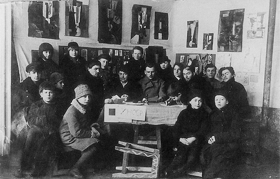 Группа УНОВИС. За столом сидят члены Творкома, слева направо: К.Малевич, В.Ермолаева, И.Гаврис, Н.Коган, Л.Лисицкий, О.Берштейн (пишет). Стоят: Е.Магрил, Л.Юдин, А.Гируцкая, Т.Меерсон; слева на переднем плане сидит И.Байтин. 1920. Фото: Музей истории ВНХУ